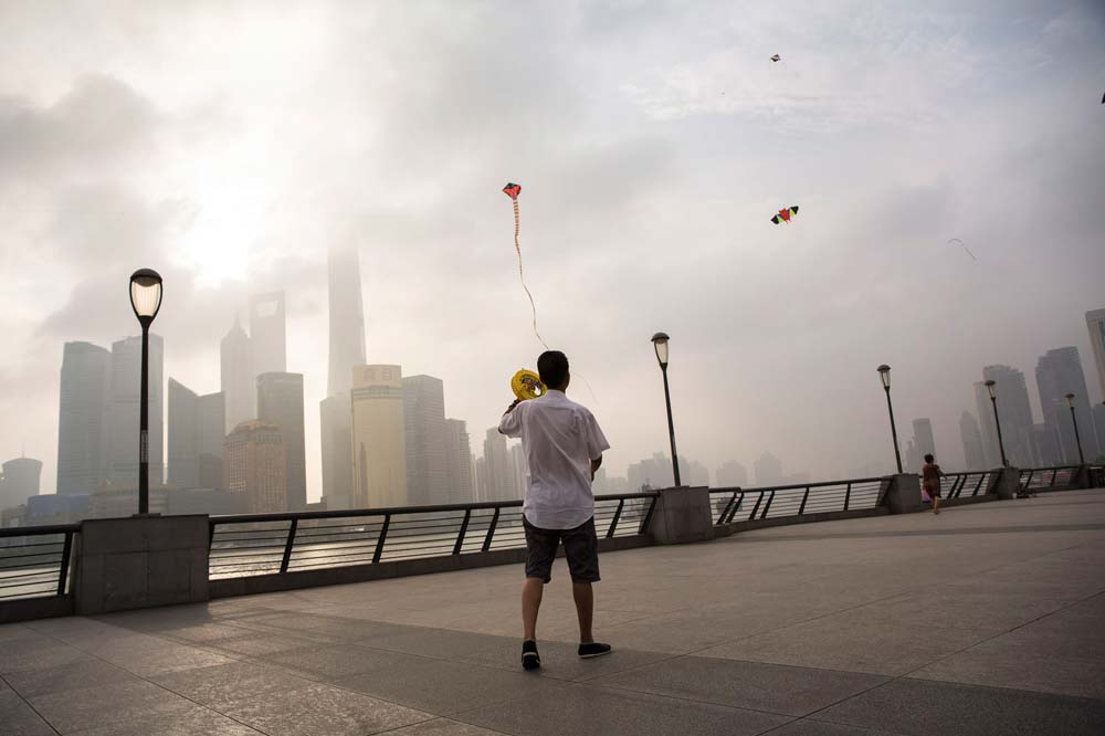 Einheimische lassen an der Uferpromenade The Bund in Shanghai ihre Drachen steigen. Im Hintergrund ragen Hochhäuser in den Morgennebel. Foto: Manuel Hauptmannl